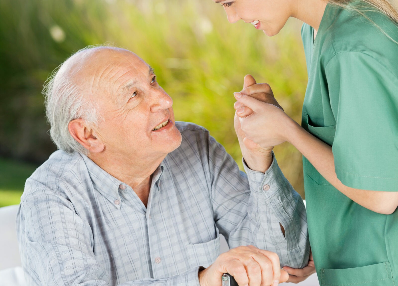 Female Caretaker Helping Senior Man To Get Up From Couch